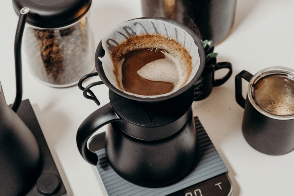 Příprava kávy v černém kovovém dripperu Hario V60 s baristickým příslušenstvím fellow, acaia váhou a miir plecháčkem na kávu