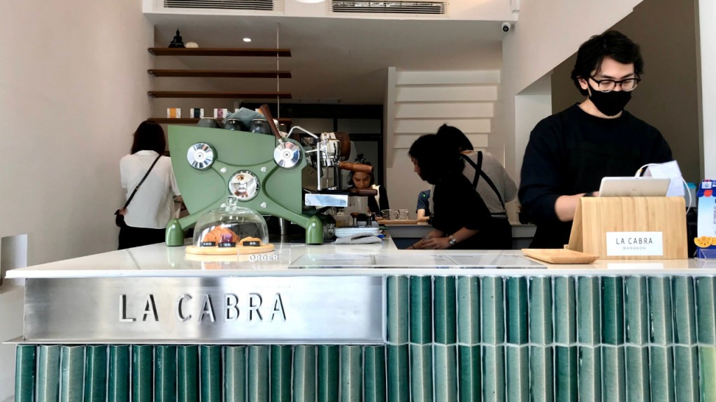 barista v kavárně La Cabra se zeleným barovým pultem a zeleným kávovarem