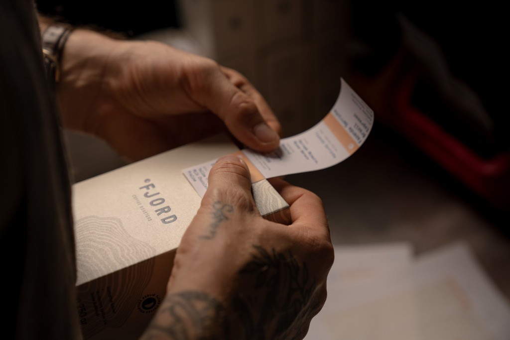 muž s tetováním na ruce lepí přelepku s informacemi o kávě na krabičku s kávou